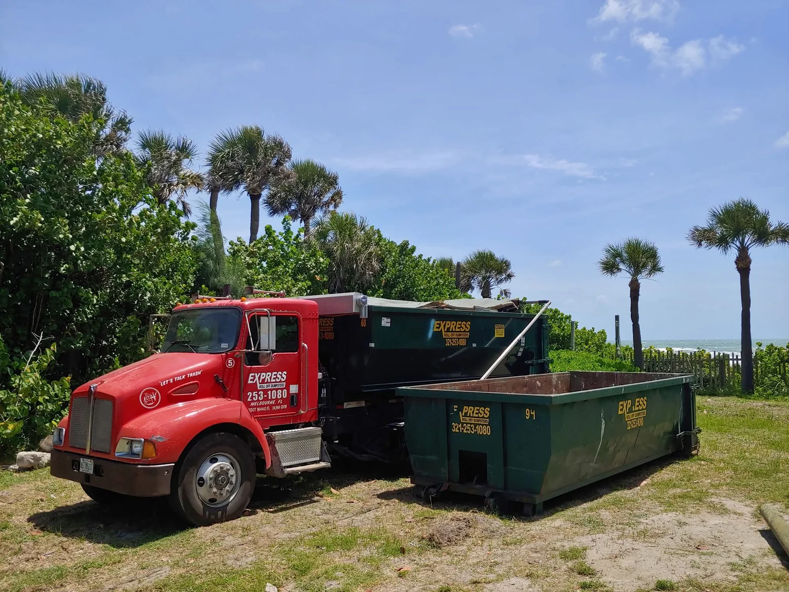 Construction crew loading demolition debris into roll off dumpster beside active renovation site
