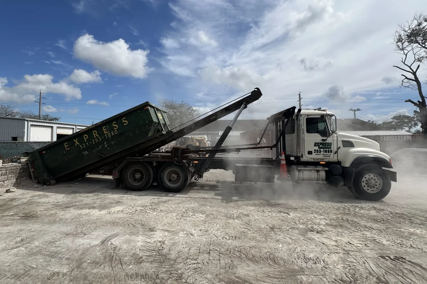 Construction crew loading demolition debris into roll off dumpster beside active renovation site