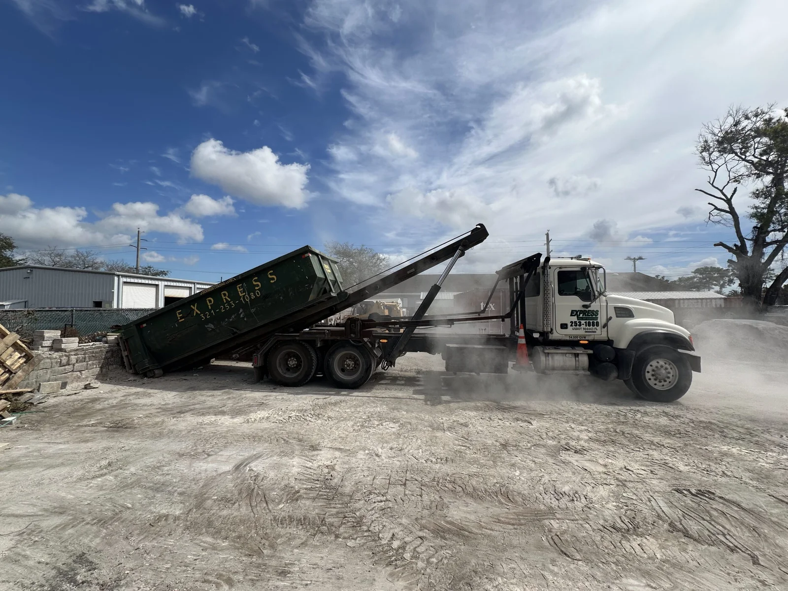 Construction crew loading demolition debris into roll off dumpster beside active renovation site